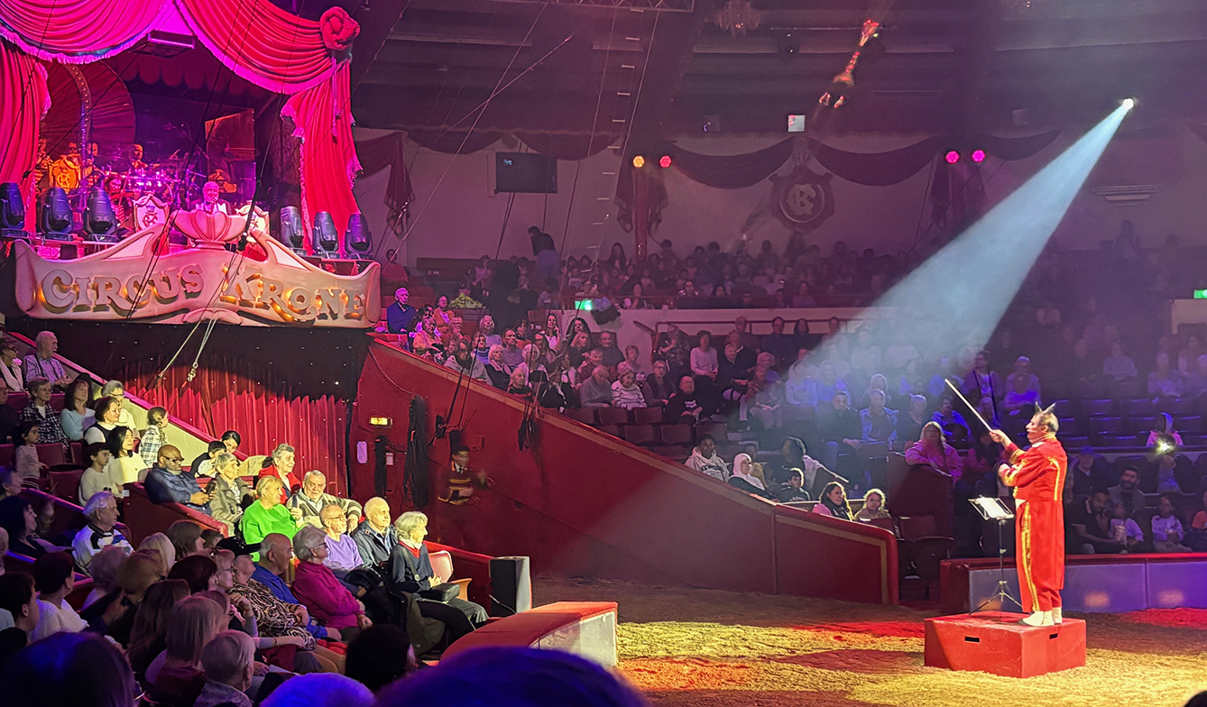 der Musikclown in rotem Frack dirigiert von der Manege aus das Krone-Orchester