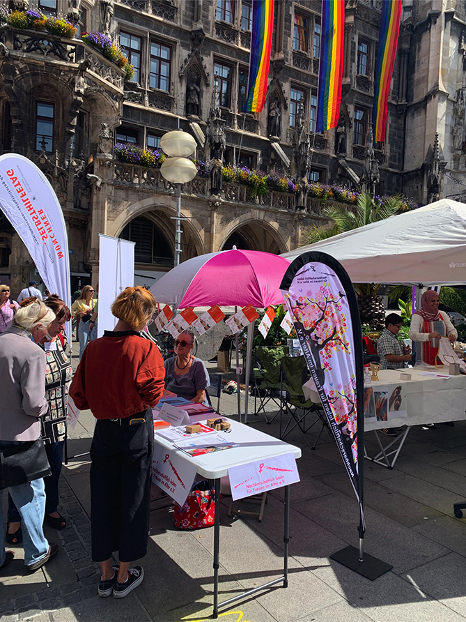 Blick auf den Infotisch mit einer Vereinsfrau und dem Rathaus im Hintergrund