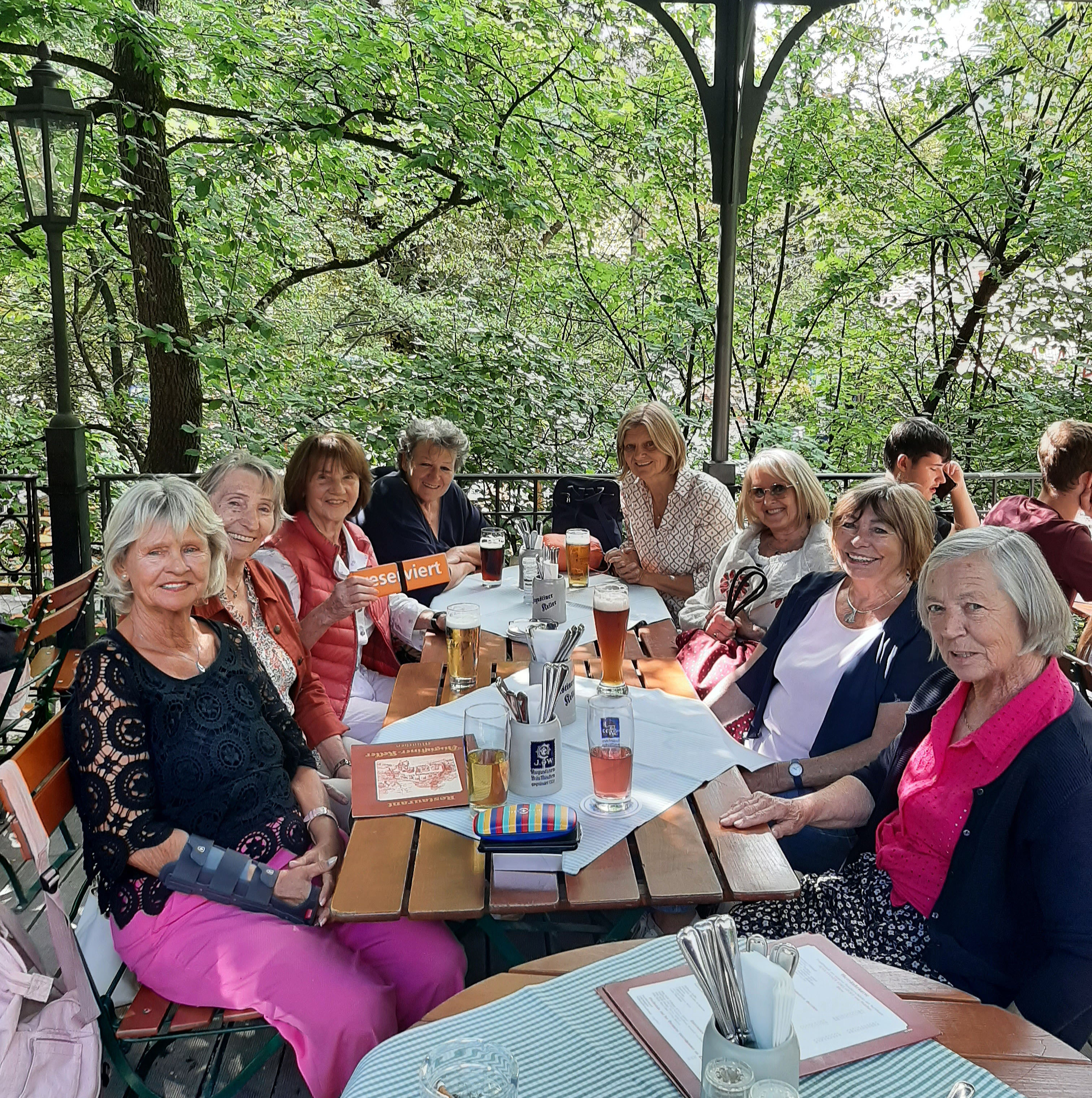 8 Damen am Biertisch vor dem Grün des Gartens