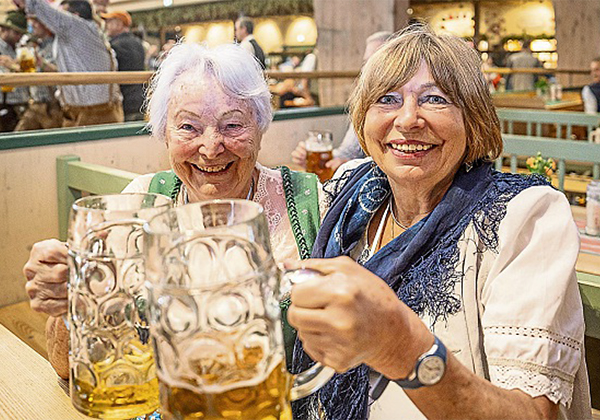 2 Frauen im Dirndl stossen am Biertisch mit einer Maß an