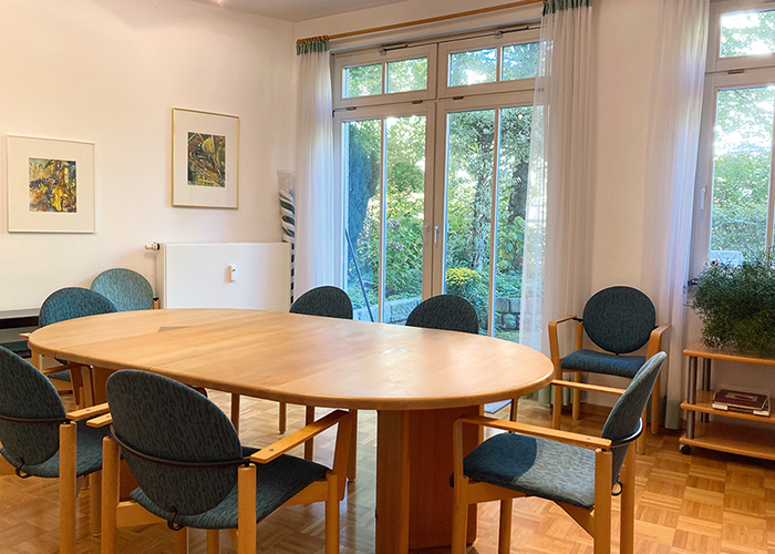 wg1: Blick in den Gemeinschaftsraums mit einem großen Tisch und großen Fenstern und Fenstertüren zum Garten